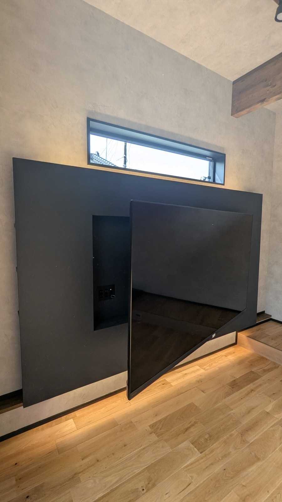 間接照明と高窓を設けたふかし壁に、角度調整できるスイングアーム式壁掛けテレビを設置。背面ニッチに配線や機器を完全隠蔽しています。